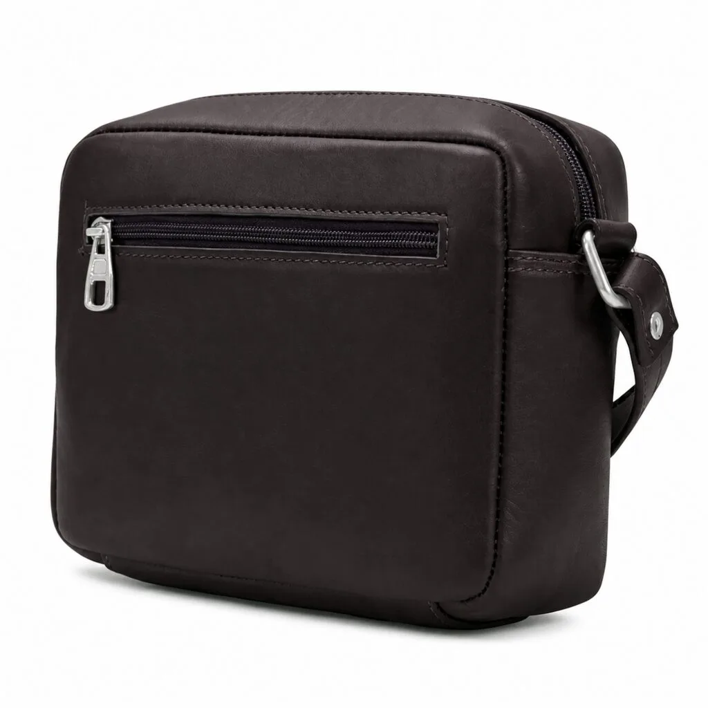 Compact espresso brown full-grain leather camera bag, boxy crossbody silhouette with a silver top zip and a horizontal front zip pocket, shown three-quarter on white.