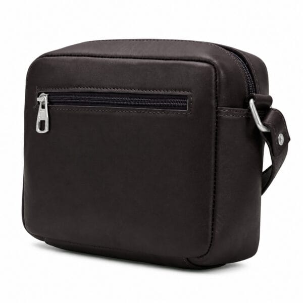 Compact espresso brown full-grain leather camera bag, boxy crossbody silhouette with a silver top zip and a horizontal front zip pocket, shown three-quarter on white.