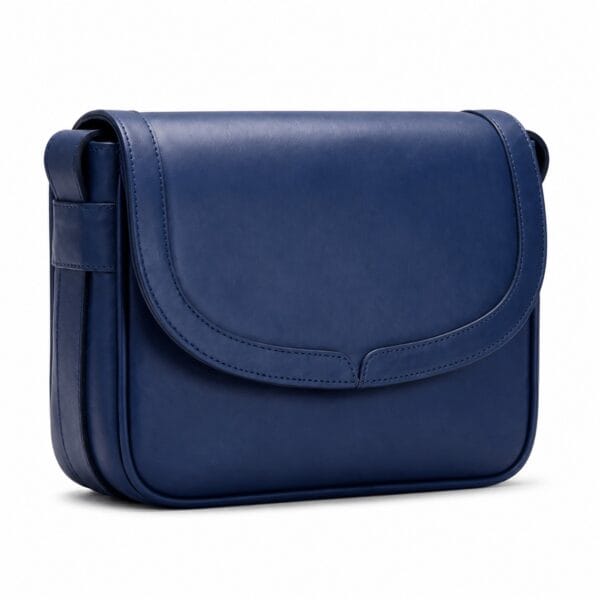 Royal blue full-grain leather flap bag with a large curved front flap, centre notch detail and an adjustable leather shoulder strap.