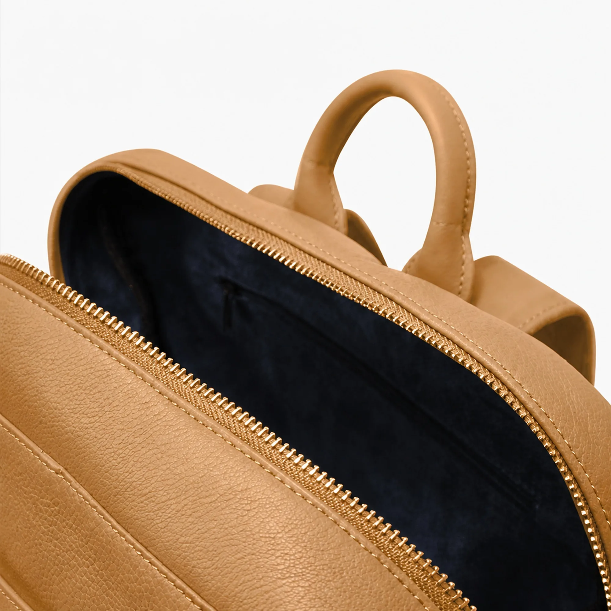 Close view of the nude beige backpack's gold-tone zip running along the navy fabric lining.