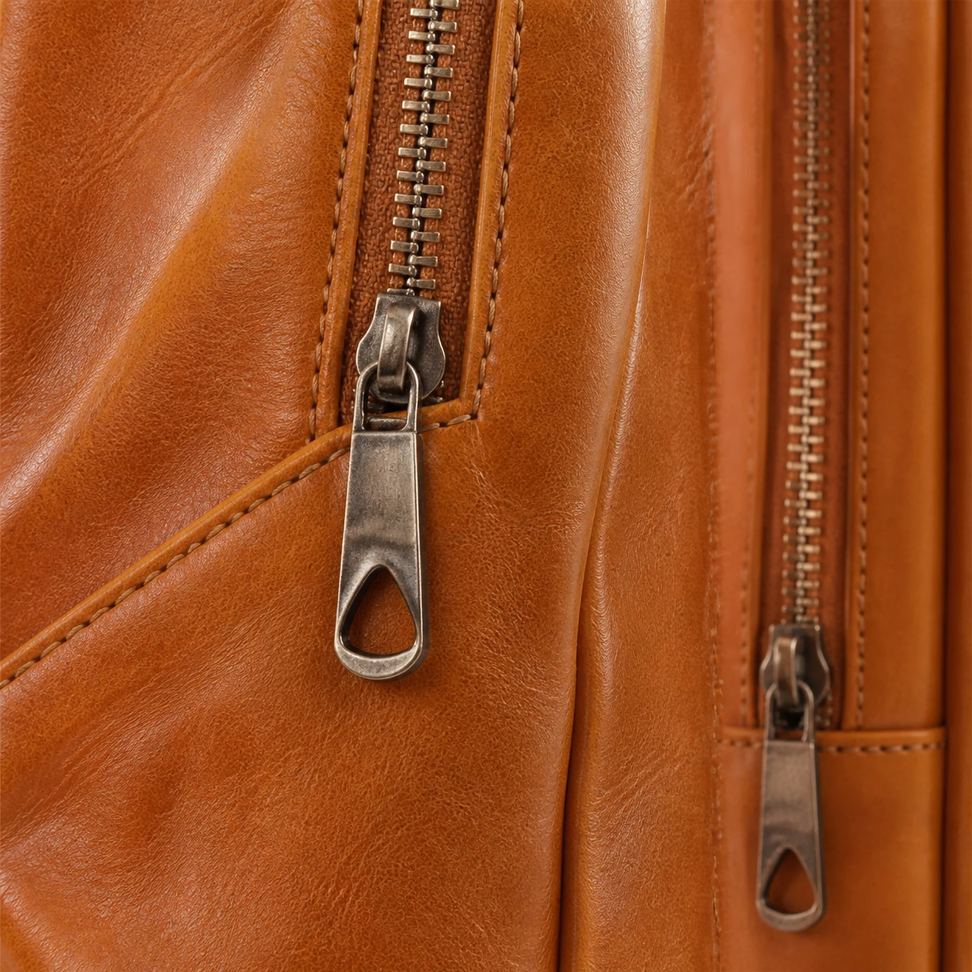 Macro of the backpack's dual zips and edge stitching against the full-grain leather.