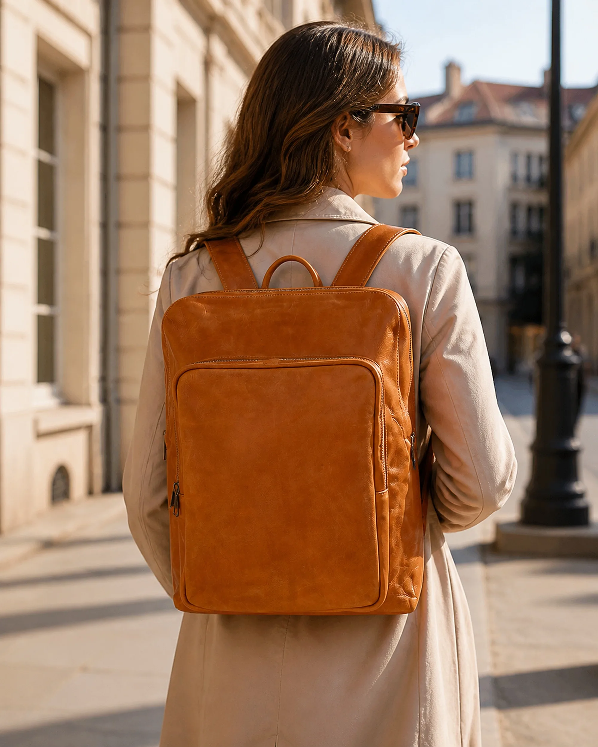 The cognac leather backpack worn on both shoulders, walking on a city street.