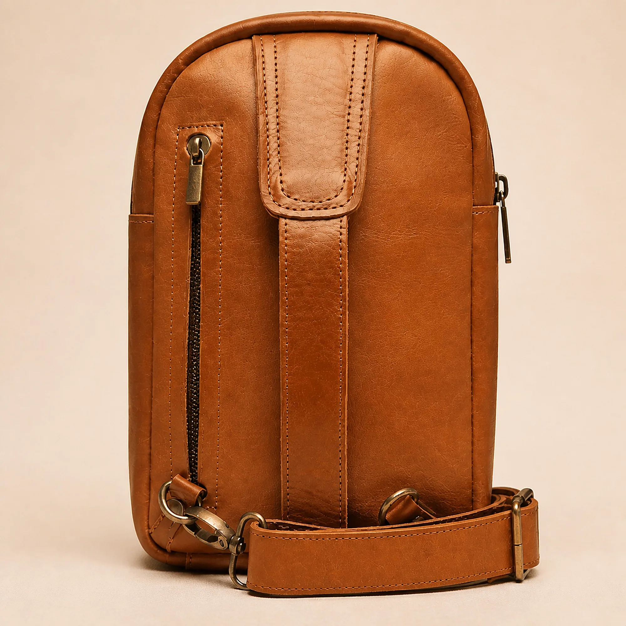 Rear three-quarter of the cognac leather sling bag with the detachable strap clipped to the antique brass D-rings.
